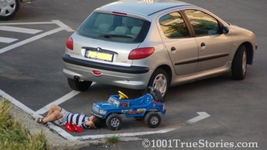 Kids imitating adults: A little boy under his toy car